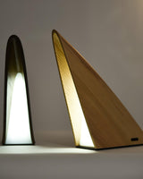 The two wood finishes of the small bedside lamp lit side by side