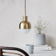 The brass pendant with a white glass tip lit above a shelf of books
