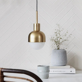 The brass pendant with a white glass tip lit above a shelf of books