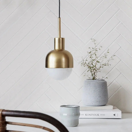The brass pendant with a white glass tip lit above a shelf of books