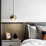 A banded pendant lit beside a bed with patterned cushions and a shelf