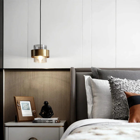 A banded pendant lit beside a bed with patterned cushions and a shelf
