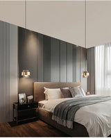A banded pendant lit on a pale bedroom wall above a wooden unit