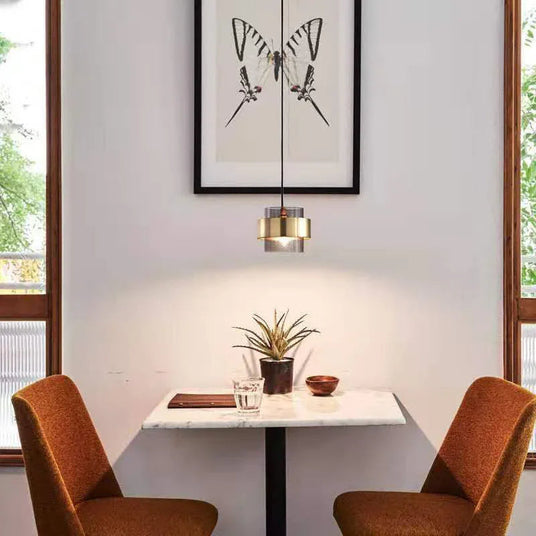 A banded pendant lit above a small cafe table with two tan chairs