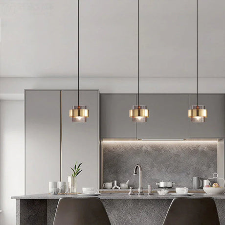 Three brass banded glass pendants in a row above a pale kitchen counter