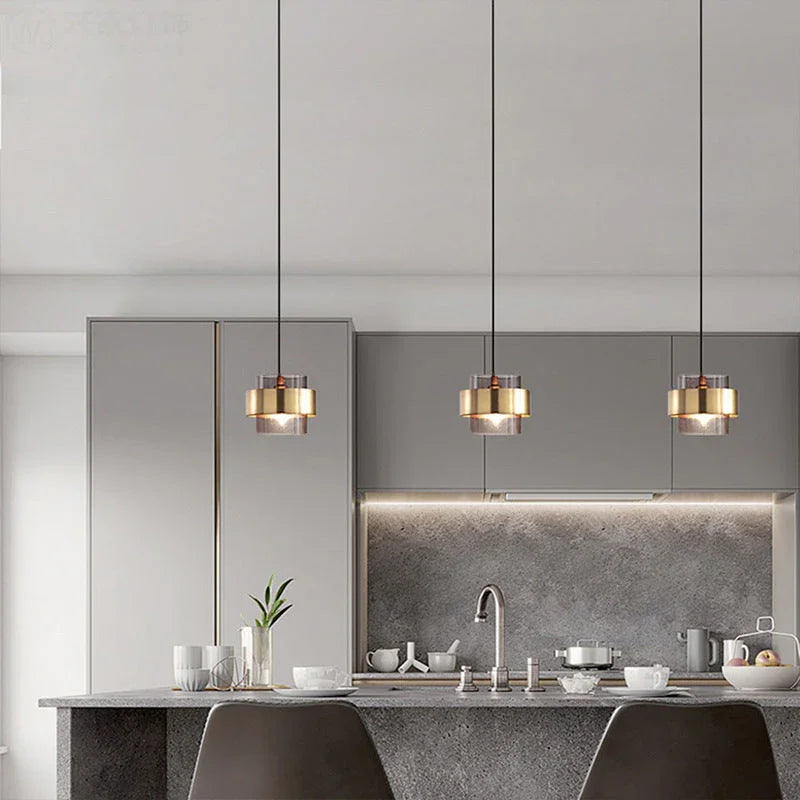 Three brass banded glass pendants in a row above a pale kitchen counter