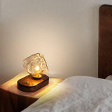 Glass ice form lamp lit on a nightstand beside a white pillow