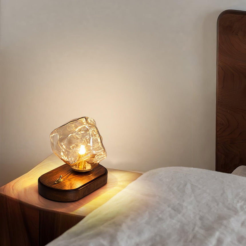 Glass ice form lamp lit on a nightstand beside a white pillow