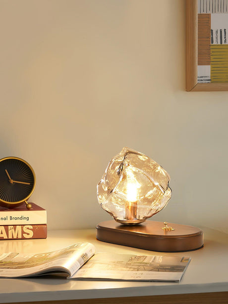 Glass ice form lamp lit on a desk beside a magazine and a clock