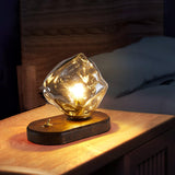 Glass ice form lamp lit on a nightstand against a wood lined wall