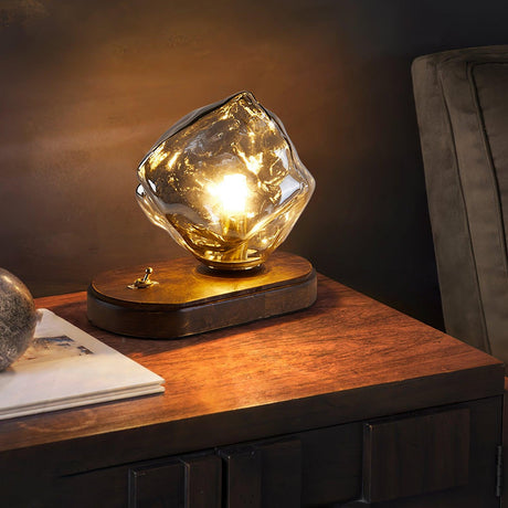 Glass ice form lamp lit on a wood desk beside an open notebook