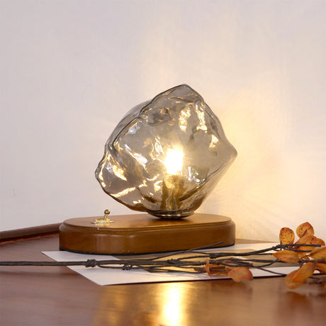 Smoke gray glass ice form lit on a desk beside dried leaves