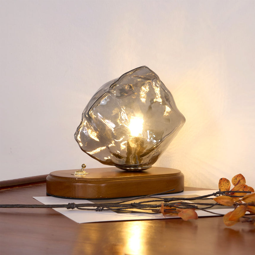 Smoke gray glass ice form lit on a desk beside dried leaves
