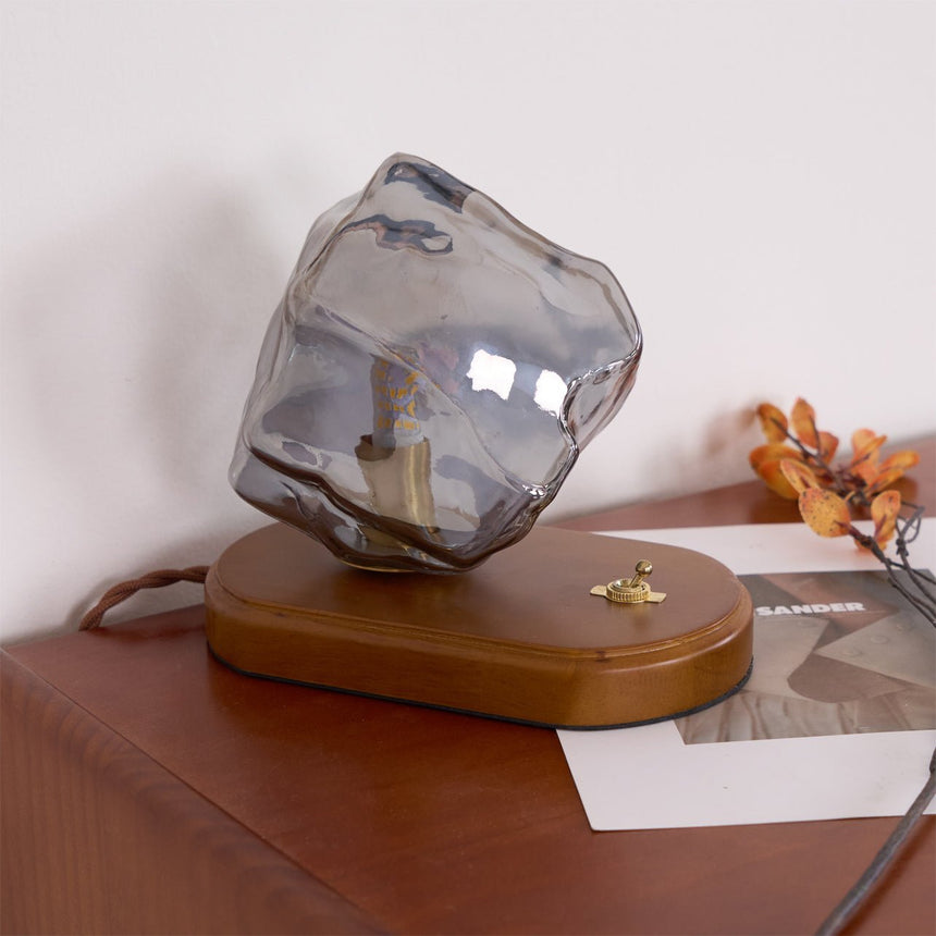 Smoke gray glass ice form unlit on a desk beside dried leaves