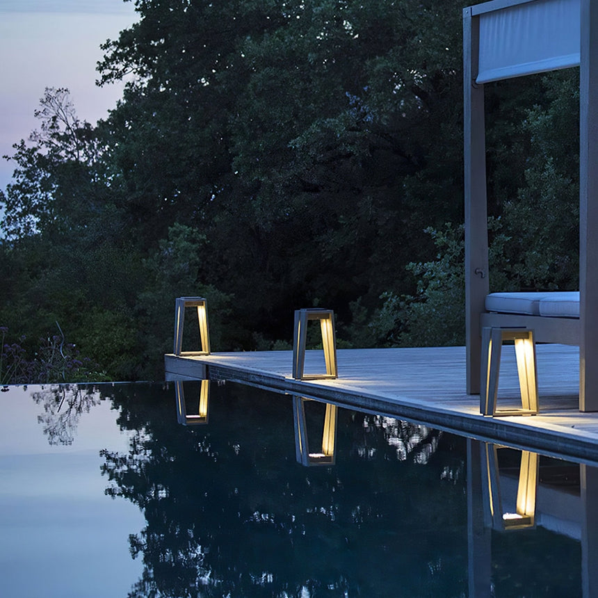 Two lit at the edge of a dark pool with trees standing behind them