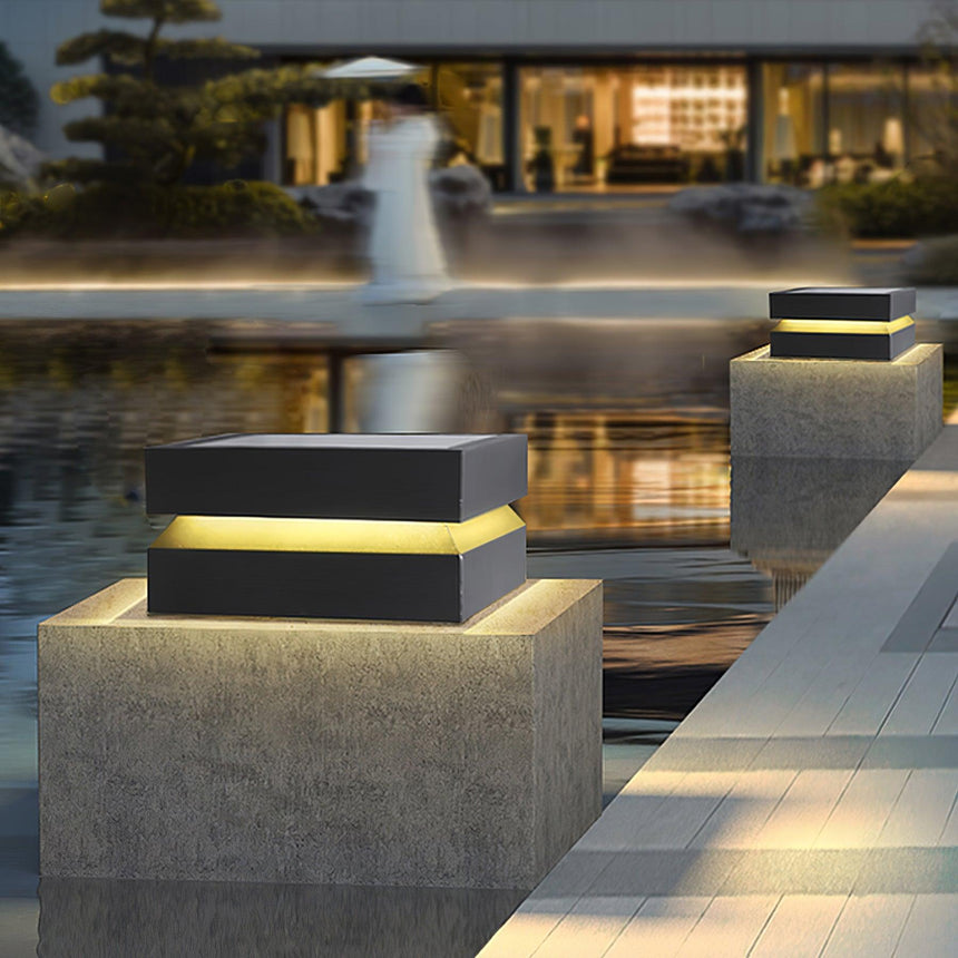 A lit cap on a pillar beside a still water feature after sunset