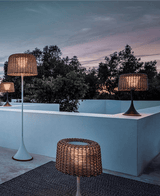 A group of the woven lamps lit on a pale terrace parapet at dusk
