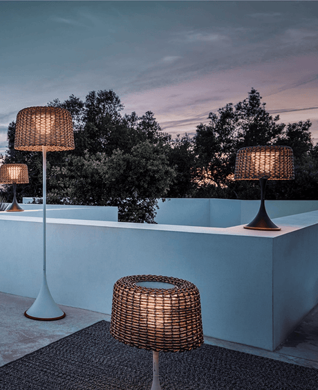 A group of the woven lamps lit on a pale terrace parapet at dusk