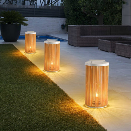 Three lit on grass beside a paved pool terrace with a sofa behind
