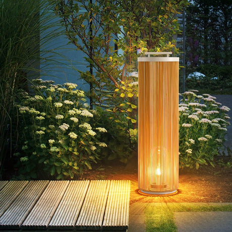 Rattan column lamp lit on decking beside white flowers in a border