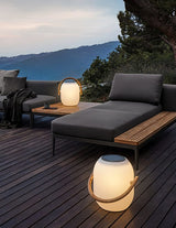 The lamp lit on a timber deck beside a daybed with hills behind it