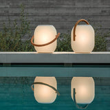 Two lamps lit on a pool edge at dusk with their reflection in the water
