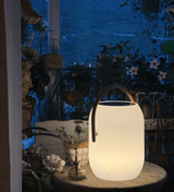 The lamp lit on a round garden table with planting and a chair behind
