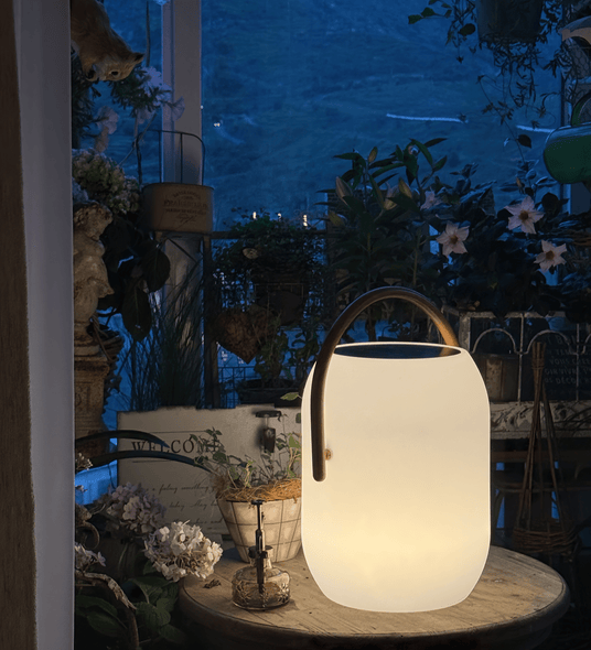 The lamp lit on a round garden table with planting and a chair behind