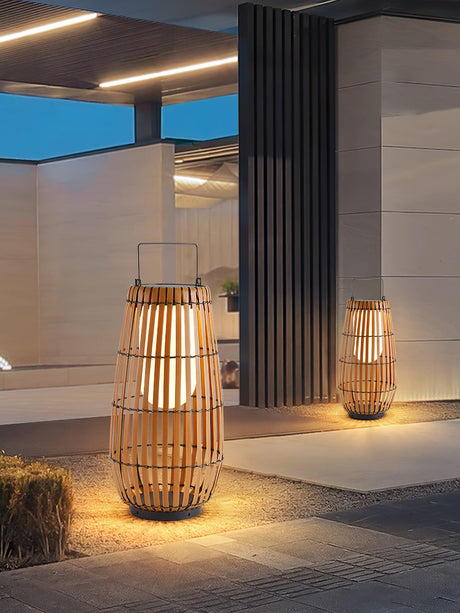 Two lanterns lit at a paved entrance beside a planted border at night