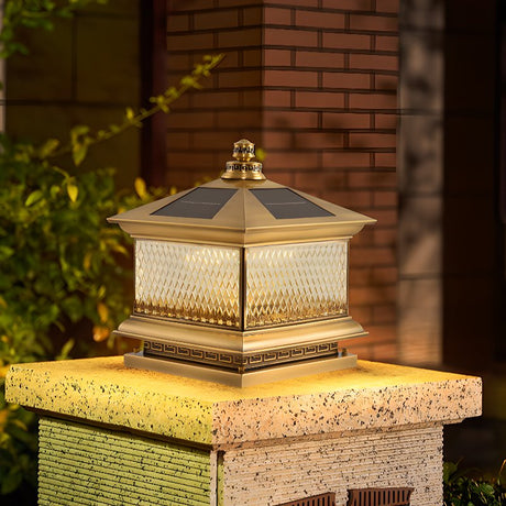 Copper toned lantern lit on a cut stone pillar beside a garden path