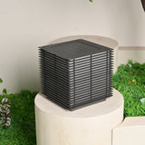 The cube unlit on a round stone plinth with a lawn and planting behind