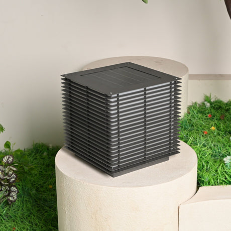 The cube unlit on a round stone plinth with a lawn and planting behind