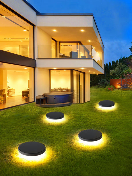 Four lit across a lawn in front of a lit modern house at dusk