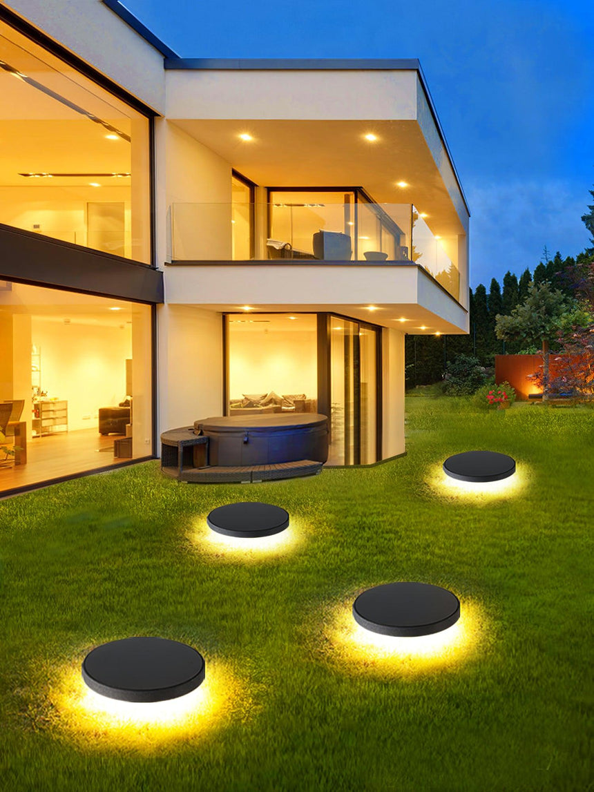 Four lit across a lawn in front of a lit modern house at dusk