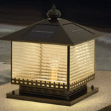 The lantern lit on a masonry pillar with planting in the evening