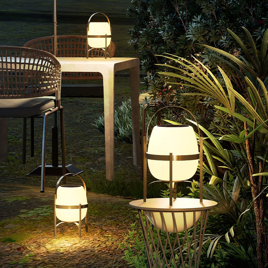 Two lamps lit among garden planting beside a table and chairs at night