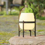 The lamp standing lit on a flat stone at the edge of a mown lawn