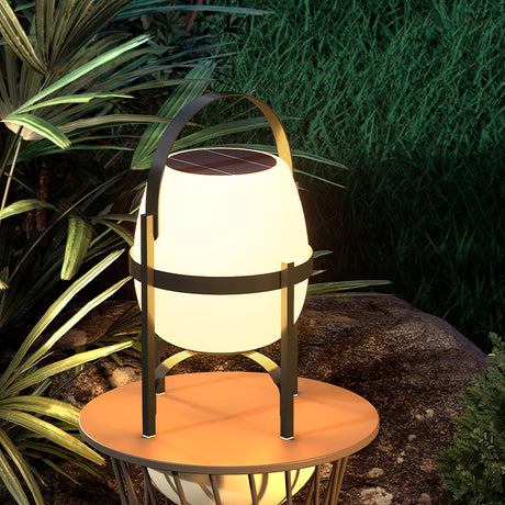 The lamp lit on a round wood table with tall planting behind it at night