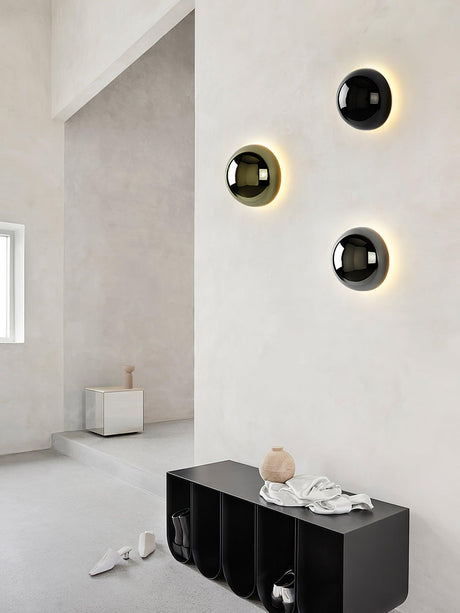 Three spheres lit on a white wall above a low black cabinet
