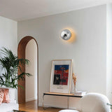 The chrome sphere lit in a hallway above a bench with a framed print and a plant