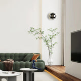 The chrome sphere above a green sofa and a vase of branches in a living room