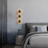 Three small spheres lit in a column beside a bed with gray linens