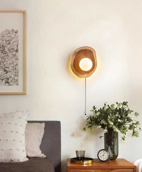 Sconce lit above a nightstand with a vase of foliage and a clock by a bed