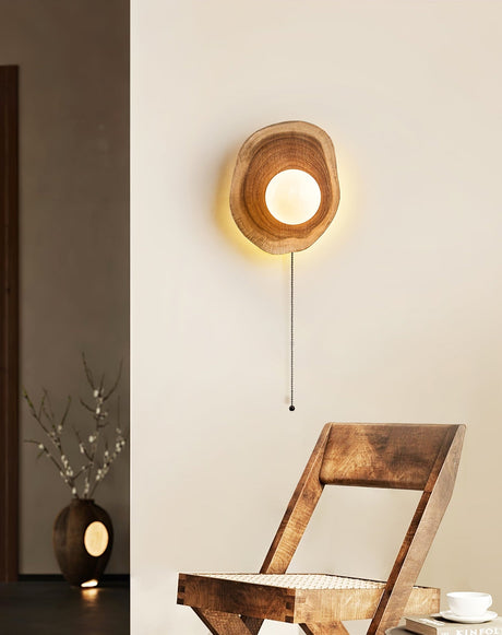 Sconce lit beside a wood chair and a narrow shelf holding a small vase