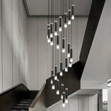 Spiral cluster of slim lit cylinders dropping beside a pale concrete staircase