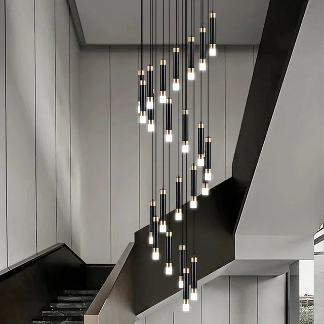 Spiral cluster of slim lit cylinders dropping beside a pale concrete staircase