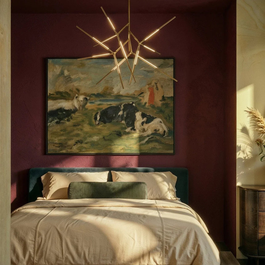 The gold version lit above a bed with pillows below a framed painting on a burgundy wall