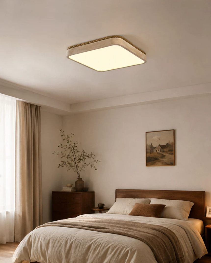 Square travertine ceiling light in a bedroom with linen curtains and a framed print