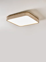 Square travertine ceiling light shown at an angle on a plain backdrop