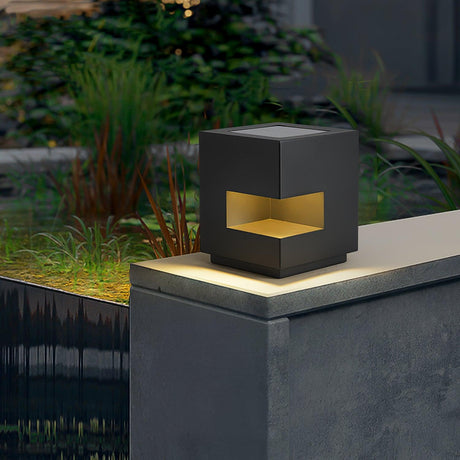 Lit cube on a pillar beside a still garden pool at the end of the day